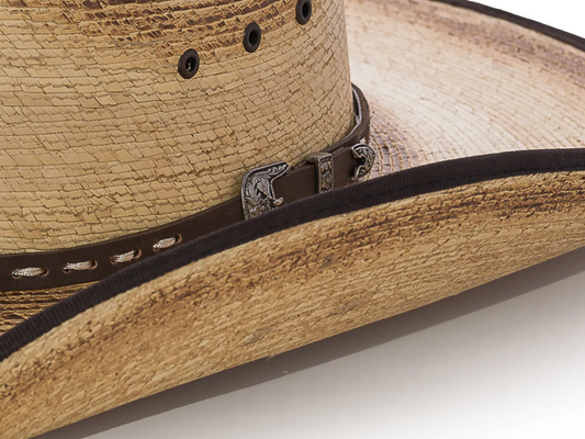 Close-up of a two-toned, distressed straw cowboy hat with a brown and white hat band and silver antique metal buckle on a white background
