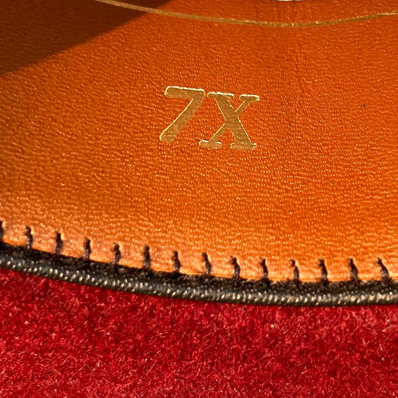 Close-up of a leather product with '7X' branding. The ruby red in the sunlight.