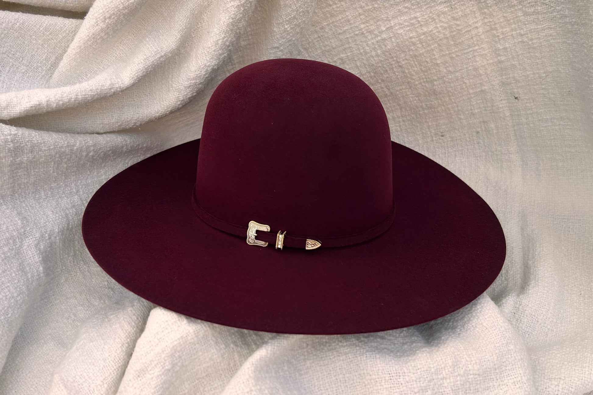 Ruby Red (Maroon) felt hat with a decorative silver with gold outline hat band on a light fabric background