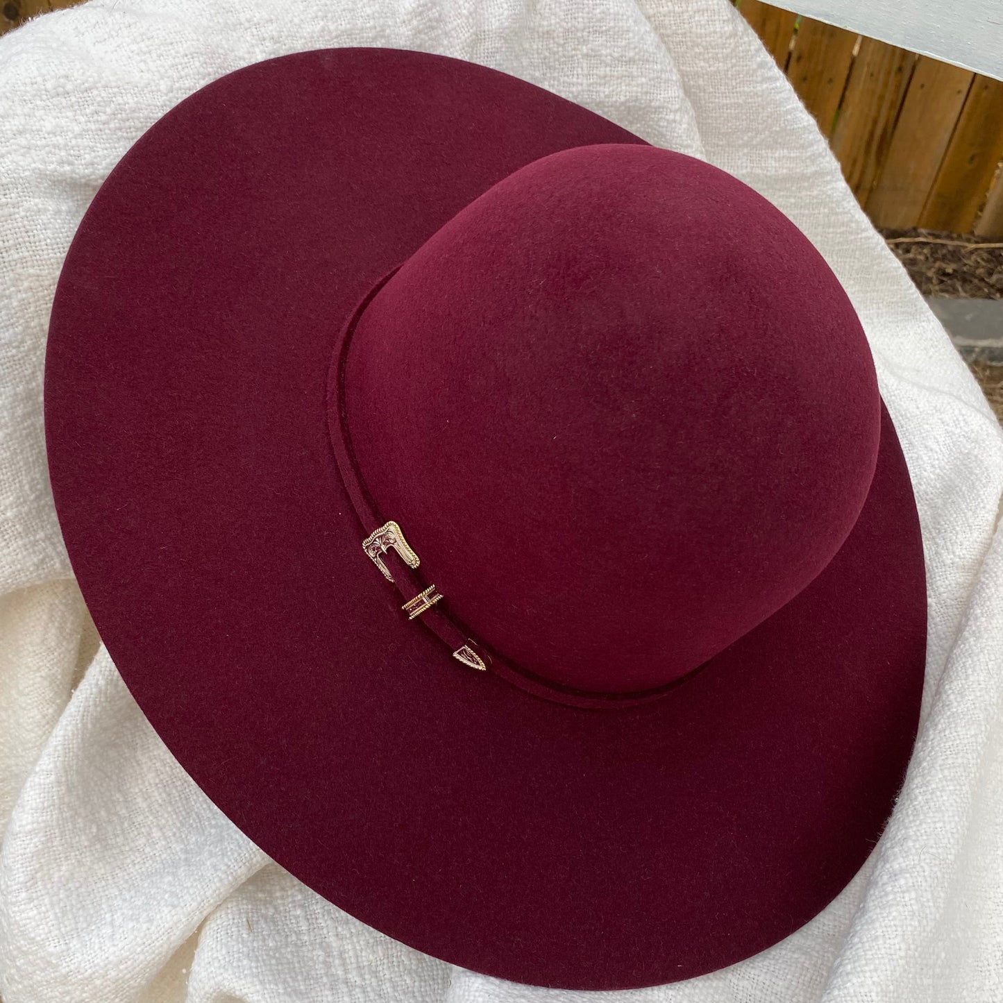 Maroon wide-brimmed hat with a silver with gold outline hat band on a white blanket